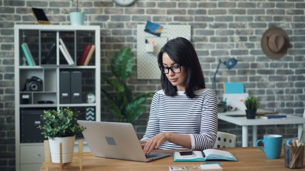 pexels-photo-22046267 Woman with glasses working on a laptop in a stylish modern office with a brick wall background.