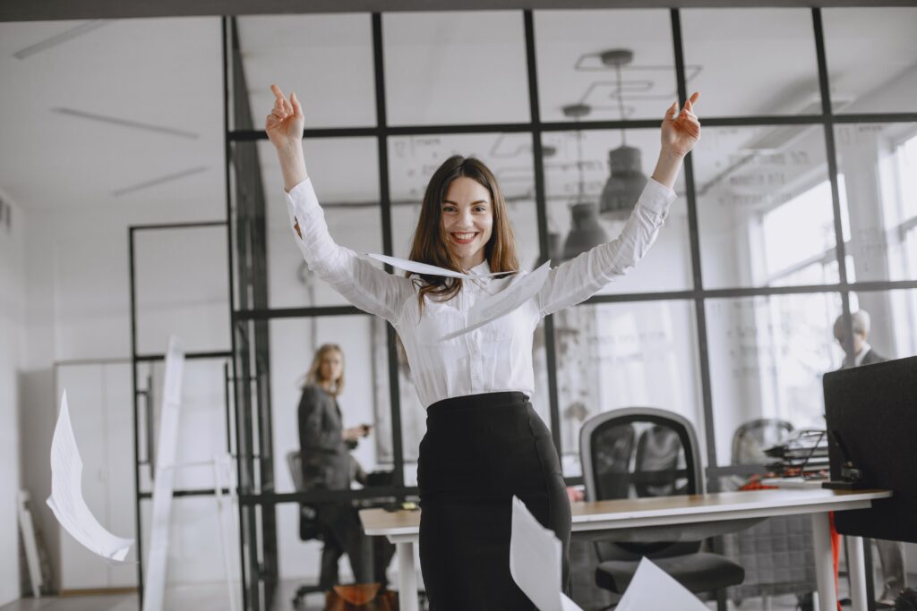 pexels-photo-4872071-4872071 Smiling businesswoman in a modern office throws papers in the air, expressing joy and success.