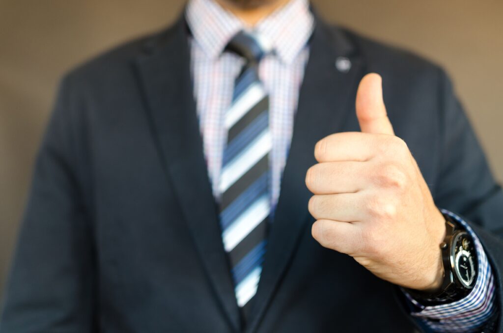 pexels-photo-653429-653429 Close-up of a businessman in a suit giving a thumbs up gesture, symbolizing success.